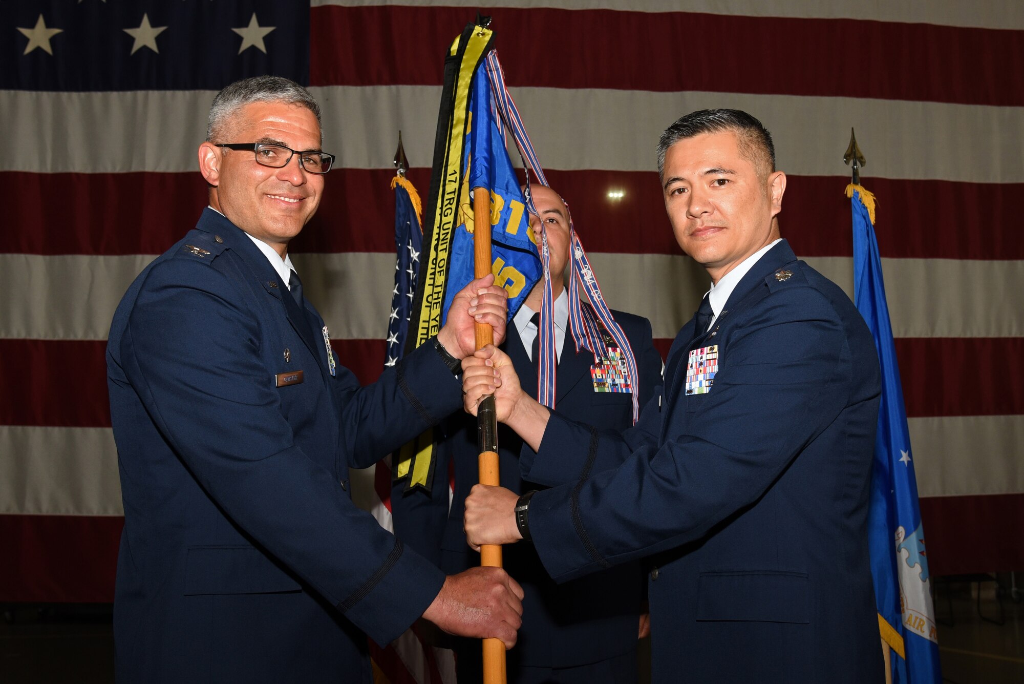 U.S. Air Force Col. Alex Ganster, 17th Training Group Commander, passes the 315th Training Squadron guideon to Lt. Col. Mark Chang, 315th TRS incoming commander, during the 315th TRS Change of Command at the Louis F. Garland Department of Defense Fire Academy High Bay on Goodfellow Air Force Base, Texas, June 1, 2018. As the 315th TRS commander, Chang is responsible for training intelligence, surveillance and reconnaissance professionals for the Air Force and other branches of the military. (U.S. Air Force photo by Staff Sgt. Joshua Edwards/Released)