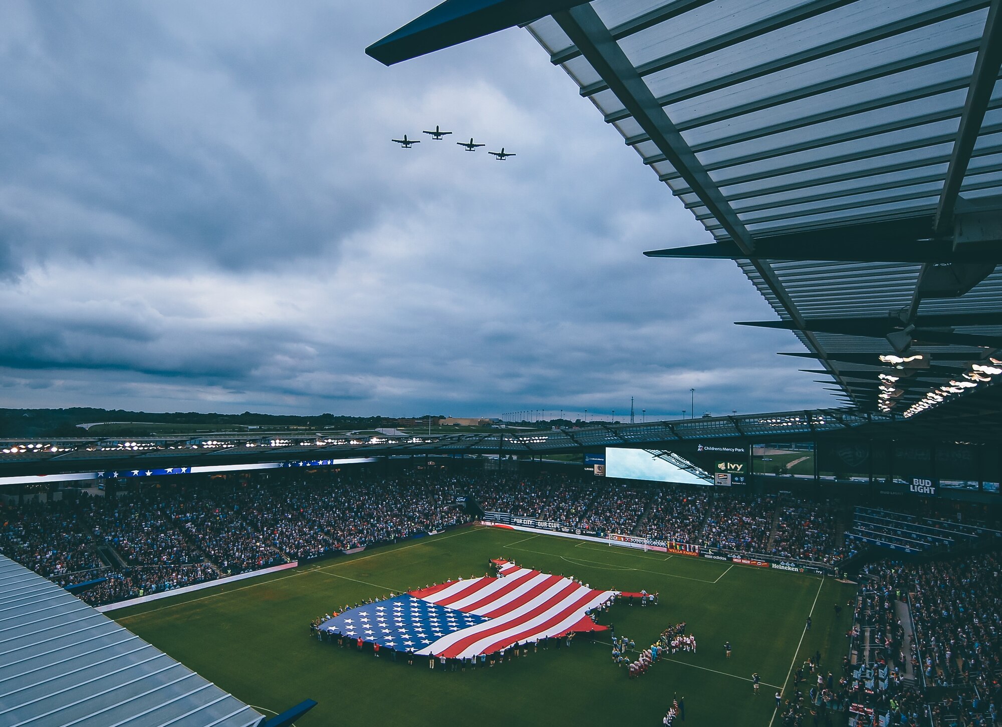 Four A-10 Thunderbolt II attack aircraft fly over Children's Mercy Park as a flag is unfurled on the field below in August 2017.
