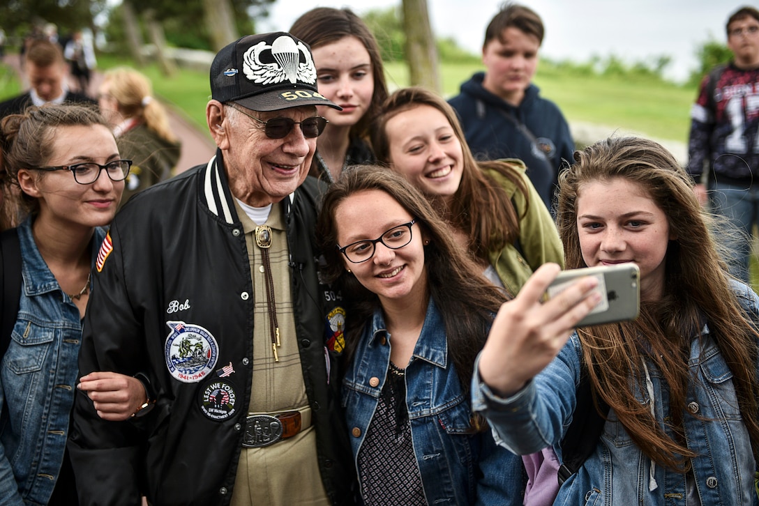 A World War II veteran smiles for a selfie with a group of schoolgirls.