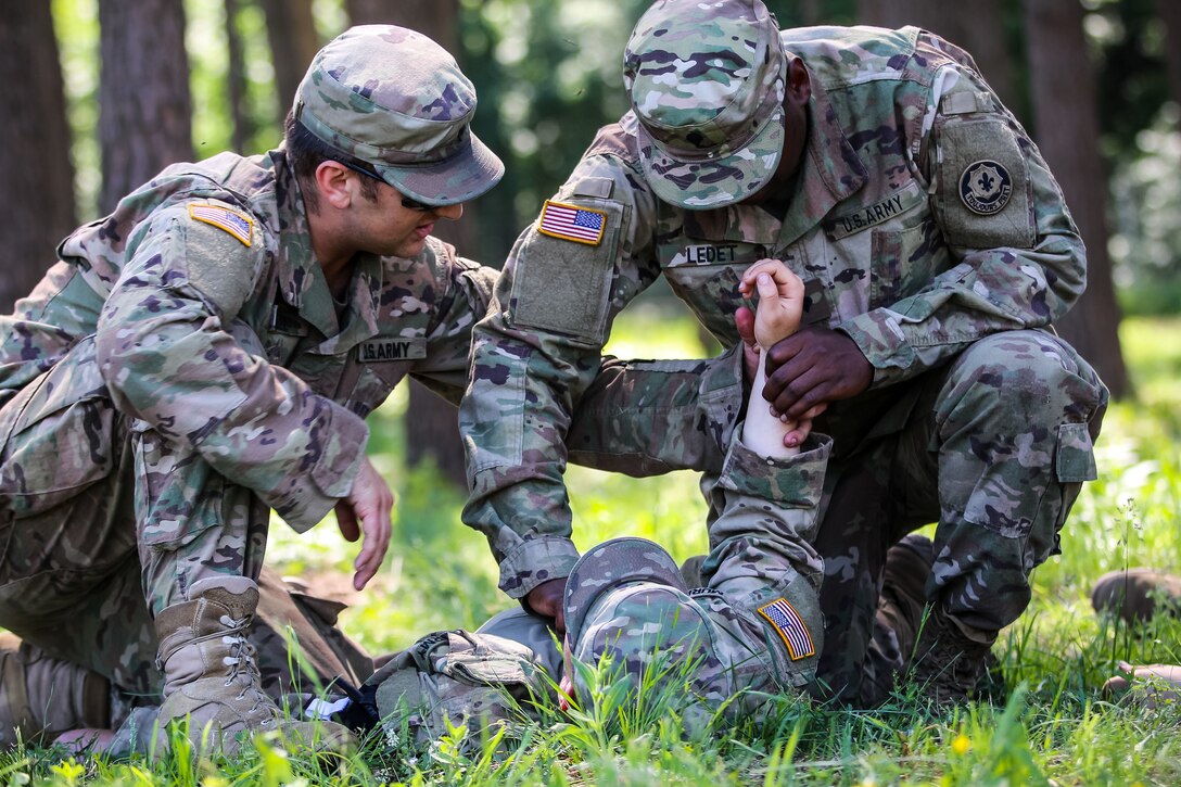 A soldier teaches another soldier how to check someone’s pulse.