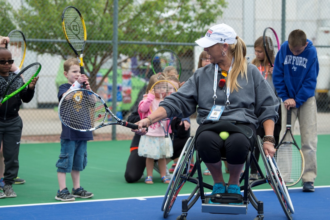 A person in a wheel chair shows children how to old a racket.