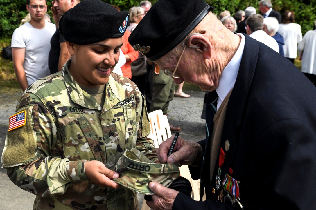 Army Sgt. Shirly Ortiz-Gomez, left, smiles as British army veteran Royston O’Neill signs her patrol cap in Tournieres, France, June 2, 2018.