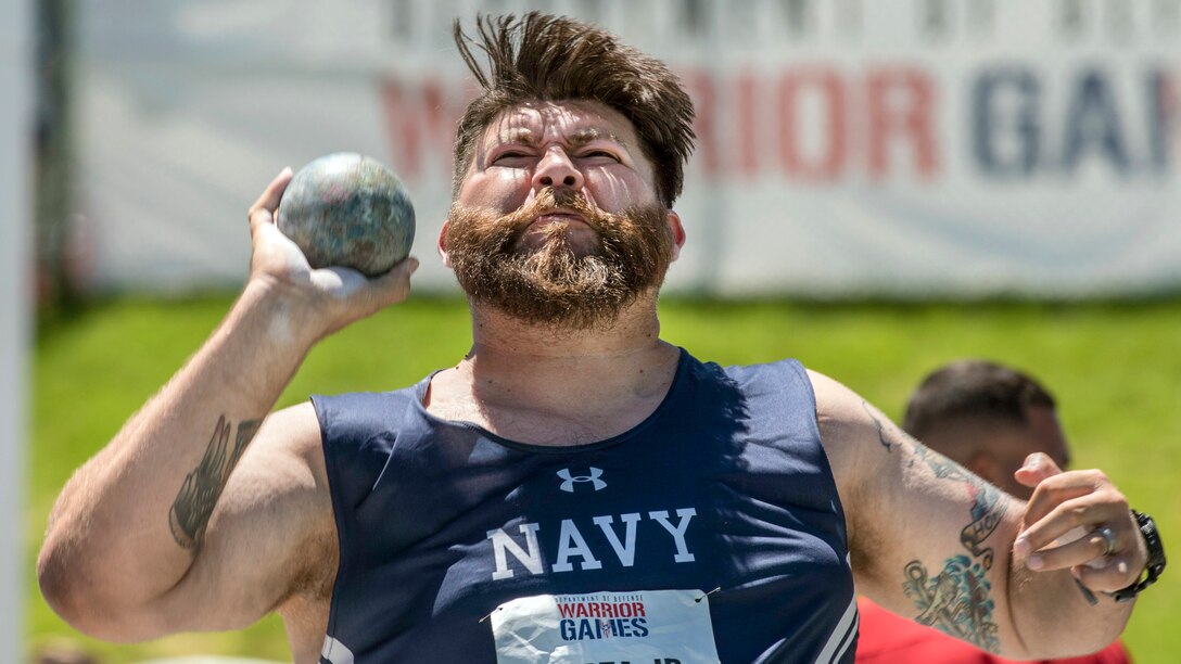 A Navy veteran winces while preparing to throw a shot put.