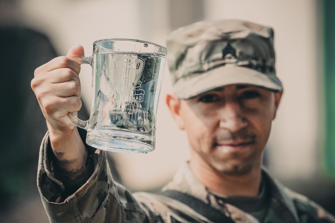 Army Sgt. Daniel Baudoin, a water purification specialist with the 240th Composite Supply Company of Baumholder, Germany, displays his battalion crest and freshly purified water he and his team produced in Poland during Exercise Saber Strike.