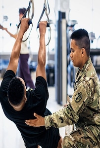 Asian male Physical Therapist wearing OCP training with a male ROTC Cadet wearing APFU inside during the daytime.