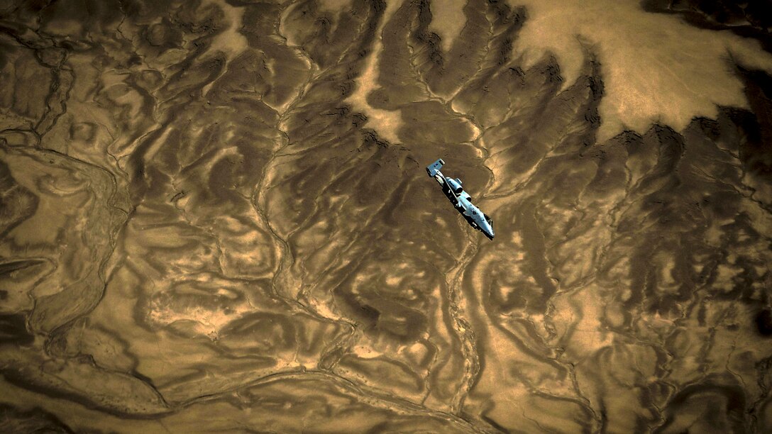 An aircraft flies over dramatic brown and tan terrain swirling that appears marbled.
