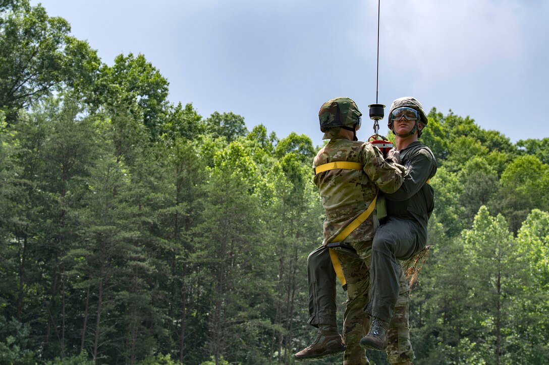 Two airmen are hoisted into a UH-60 Black Hawk helicopter.