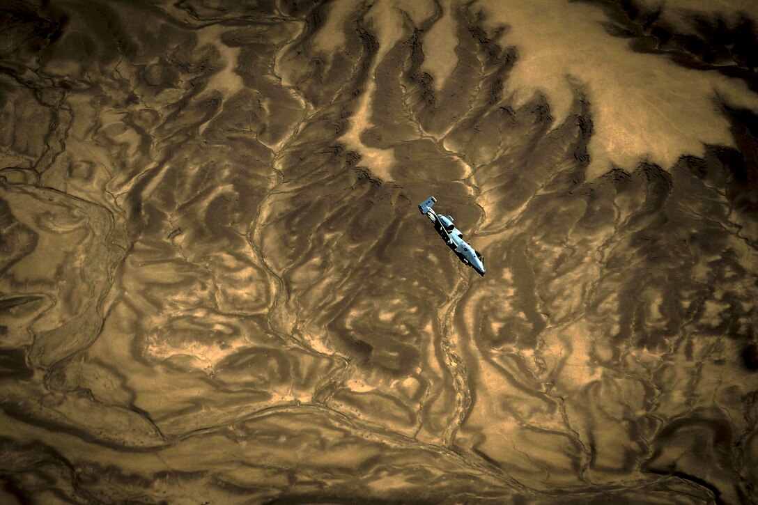 An aircraft flies over dramatic brown and tan terrain swirling that appears marbled.
