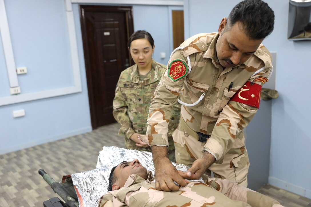 A U.S. soldier observes an Iraqi army soldier demonstrating how to apply a gauze bandage.