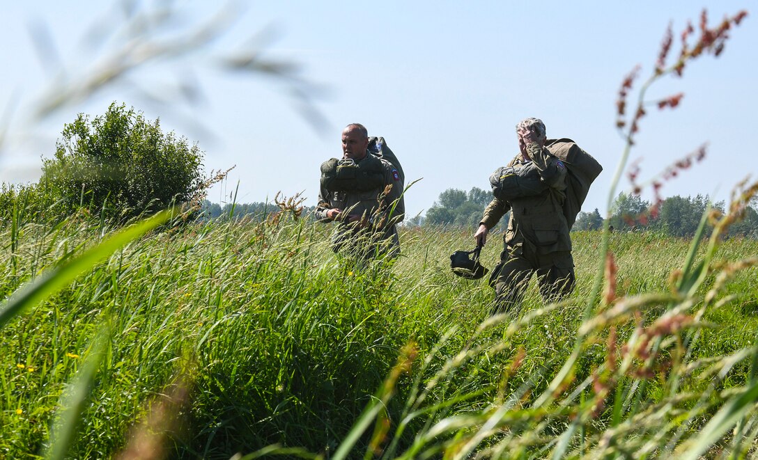 Paratroopers walk through thick brushes of grass from the landing zone