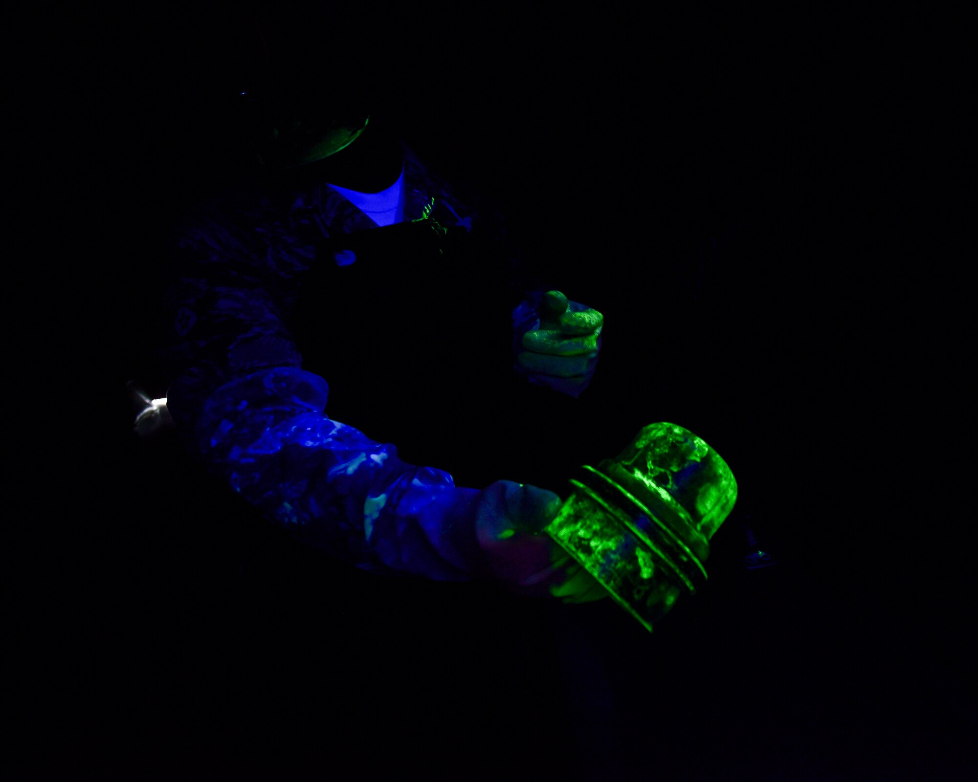 A U.S. Air Force nondestructive inspection specialist from the 325th Maintenance Squadron inspects a metal component covered in fluorescent chemicals under a black light at Tyndall Air Force Base, Fla., May 23, 2018.  Fluorescent chemicals are used to help identify small cracks or stresses on metal equipment and systems that may lead to accidents. (U.S. Air Force photo by Senior Airman Cody R. Miller/Released)