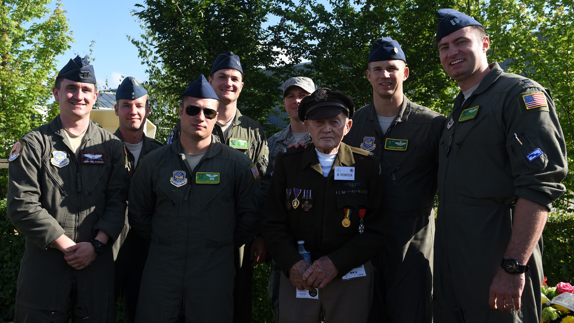 Pilots pose in flight suits for photo along side World War 2 D-Day survivor wearing world war 2 uniform and bomber jacket.