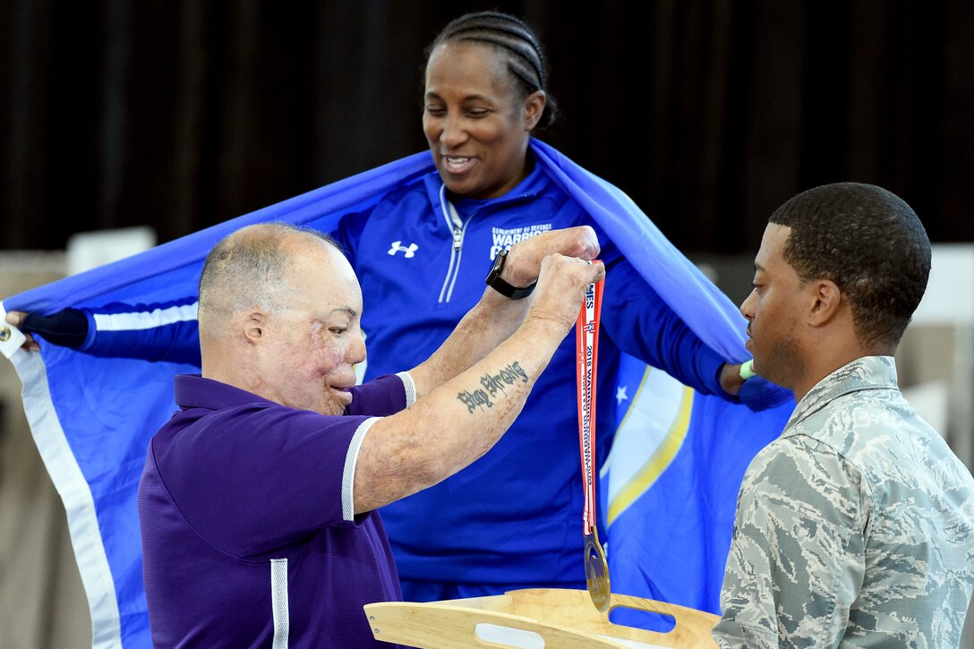 Two people pick up a medal to give it to an athlete.