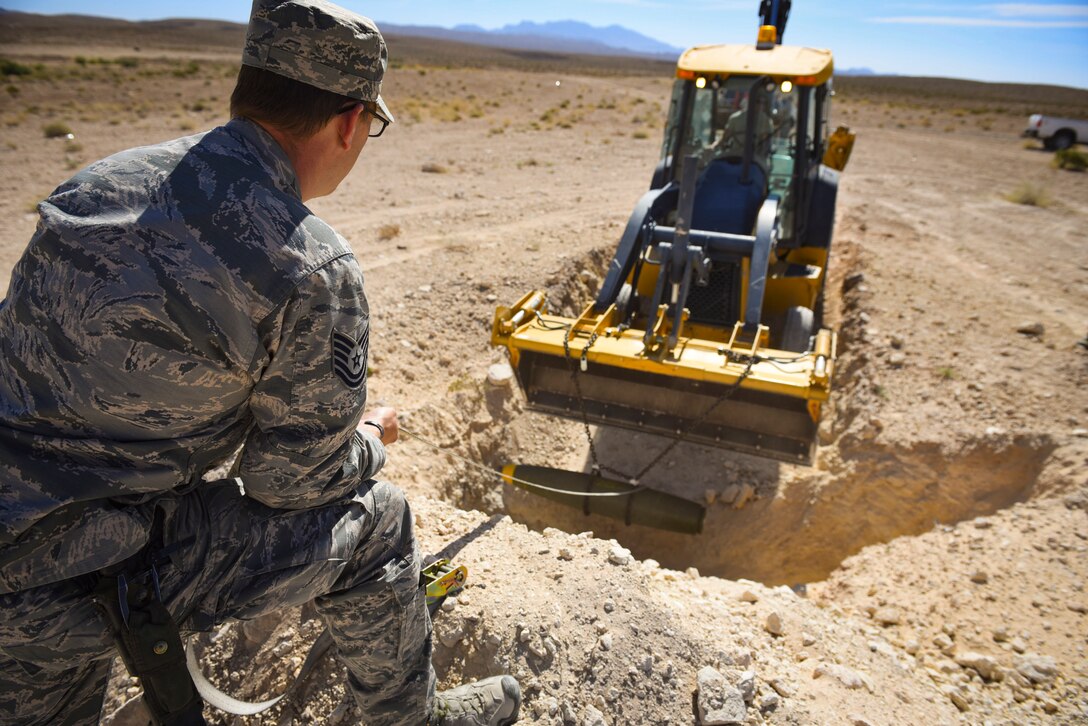 Tech. Sgt. Robert Brousseau, 99th Civil Engineer Squadron explosive ordnance disposal technician, guides a Mark 82 bomb into a hole during an ammunition disposition request at Nellis Air Force Base, Nevada, May 31, 2018. EOD technicians buried the 500-pound Mark 82 bomb underground and then covered it with dirt to minimize the blast radius of fragmentation and debris. (U.S. Air Force photo by Airman 1st Class Andrew D. Sarver)