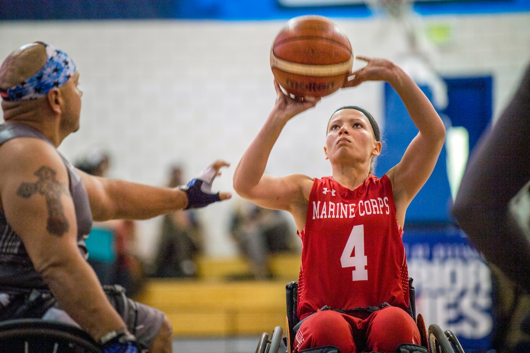 An athlete holds a basketball up before shooting, as an opponent reaches to try to block her.