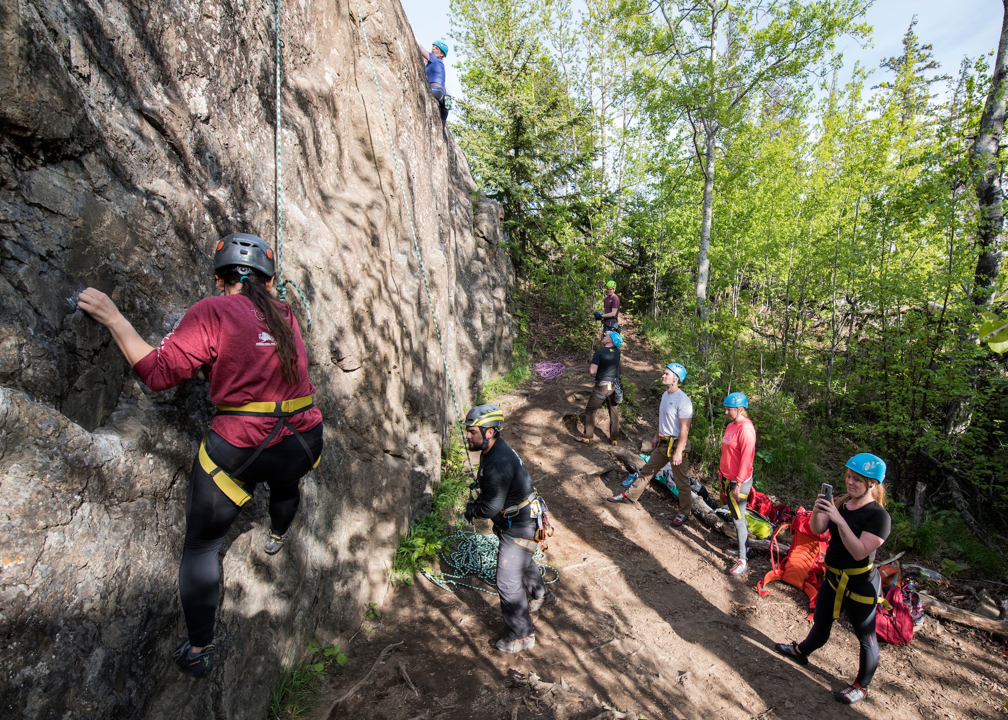 A group of climbers look on and cheer as two climbers in their group ascend during an Outdoor Adventure Program rock-climbing trip at Pivot Point Trail near Anchorage, Alaska, May 31, 2018. The OAP offers low-cost opportunities for the Joint Base Elmendorf-Richardson community to explore Alaska while also supporting the development of mission-ready military families and members.
