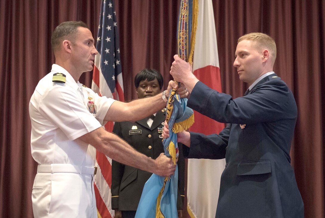 Two military officers grasp a flag during a change of command ceremony.