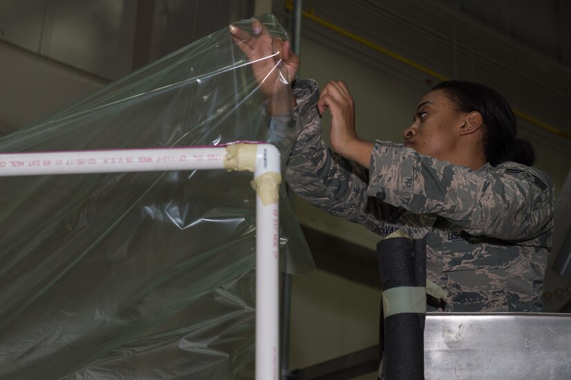 U.S. Air Force Staff Sgt. Raven Savage, 1st Maintenance Squadron low observable structural maintenance  craftsman, lays a plastic sheet over a portable paint booth at Joint Base Langley-Eustis, Virginia, March 1, 2018.