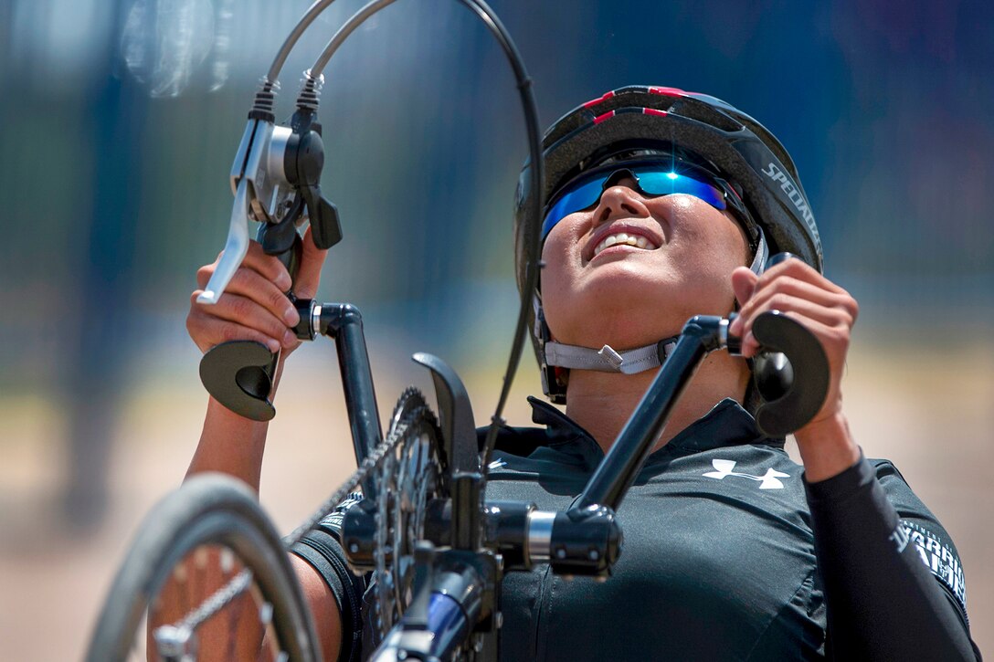 A soldier's face shows strain as she drives a handcycle up a hill.