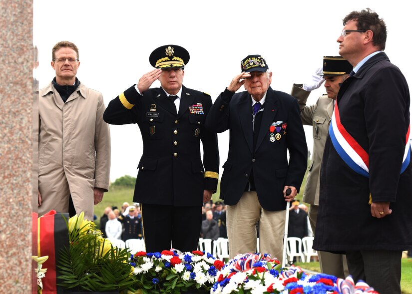 D-Day veteran John Roman, center, and Army Maj. Gen. Mark W. Palzer, commander of the 79th Theater Sustainment Command, center left, salute for the playing of French and U.S. “Taps” during the Utah Beach Federal Monument Ceremony in Sainte-Marie-Du-Mont, France.