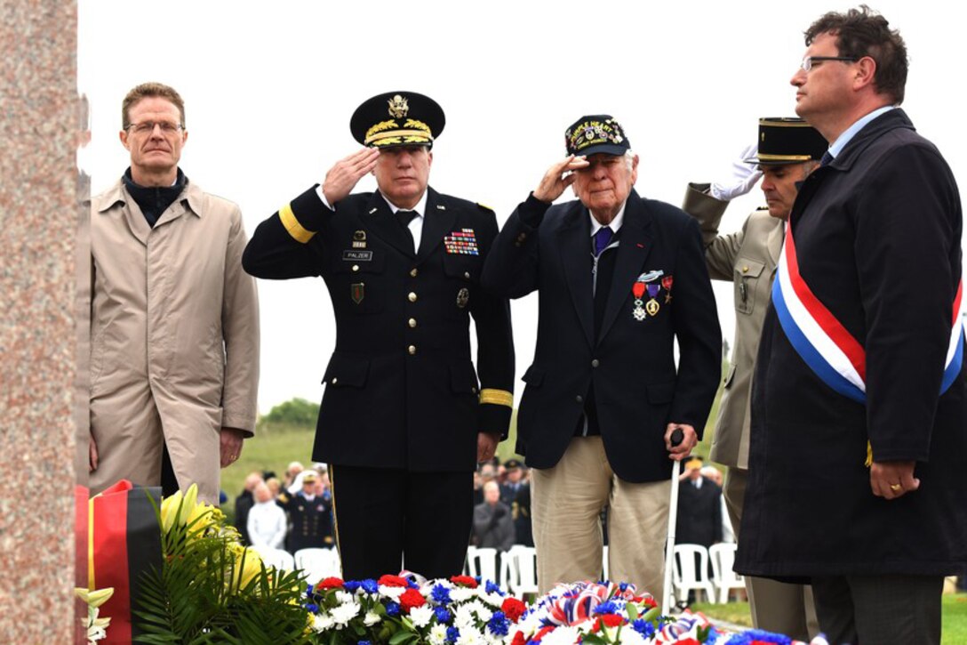 Service members and a veteran salute at a memorial.
