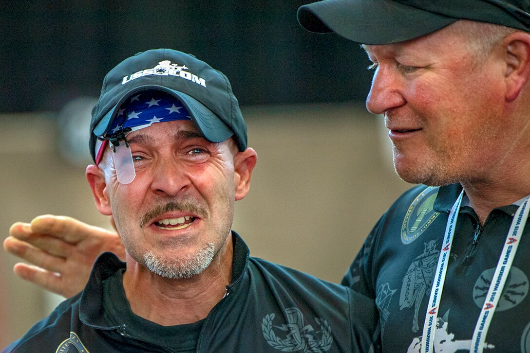 An athlete smiles as another man puts his arm around him.