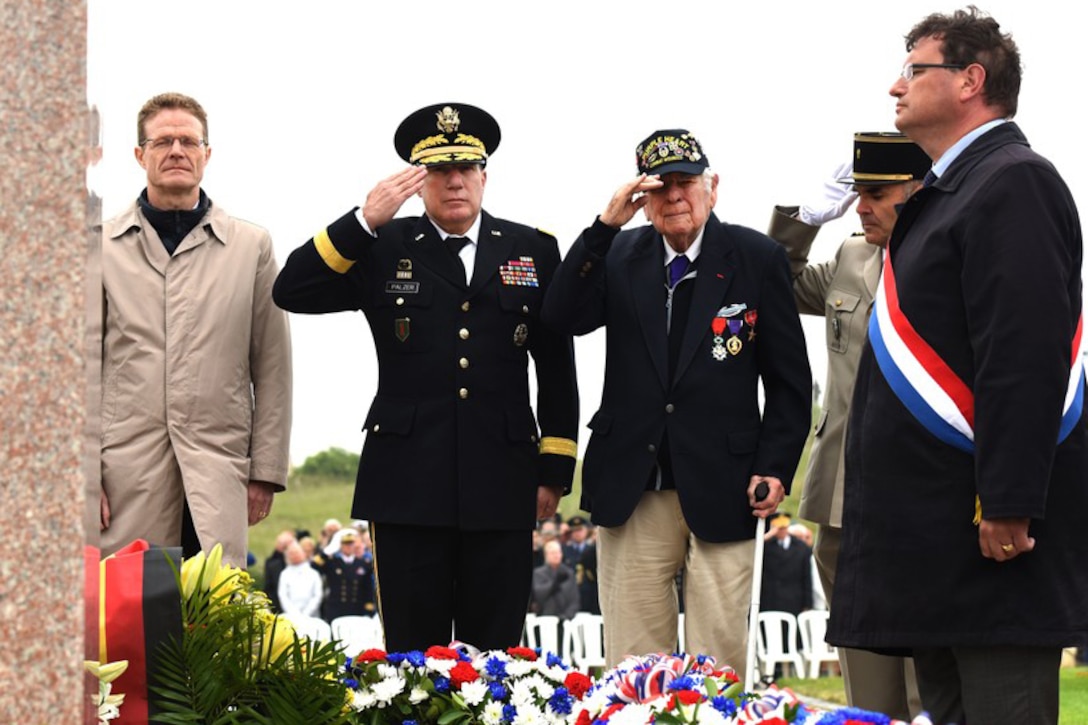 Service members and a veteran salute at a memorial.