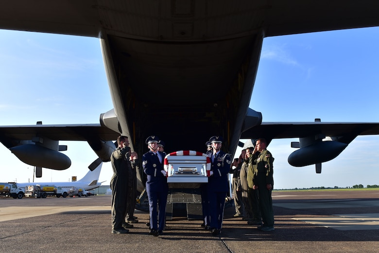 Men carry a coffin, while other men salute them as they walk by.