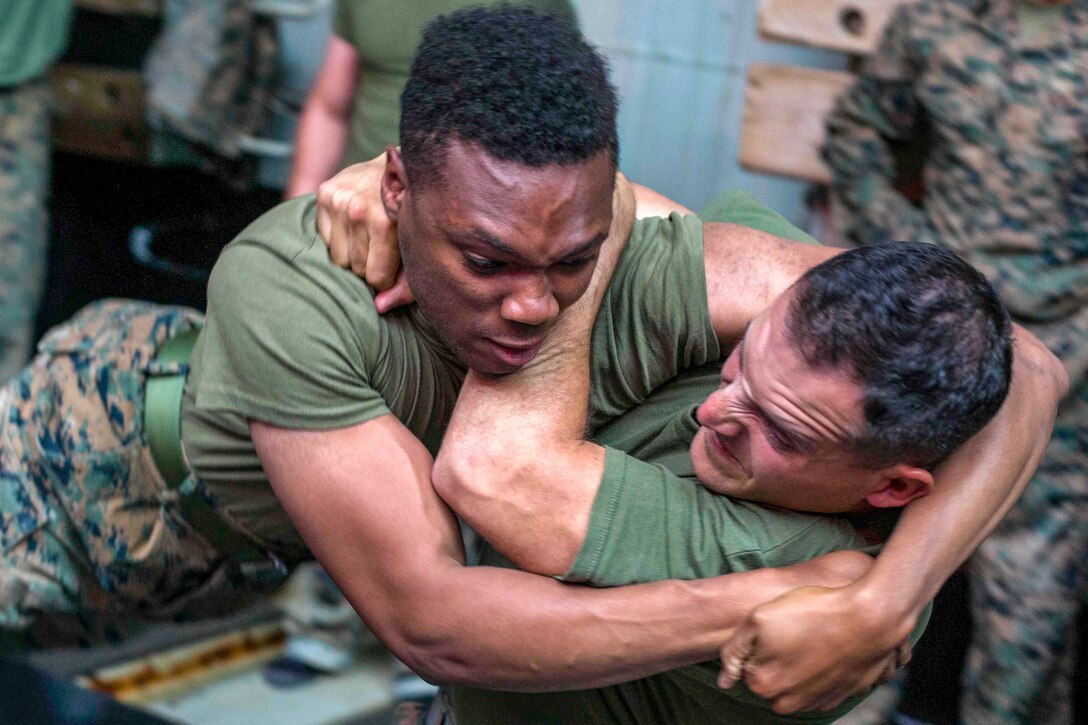 Two Marines grimace while wrestling.