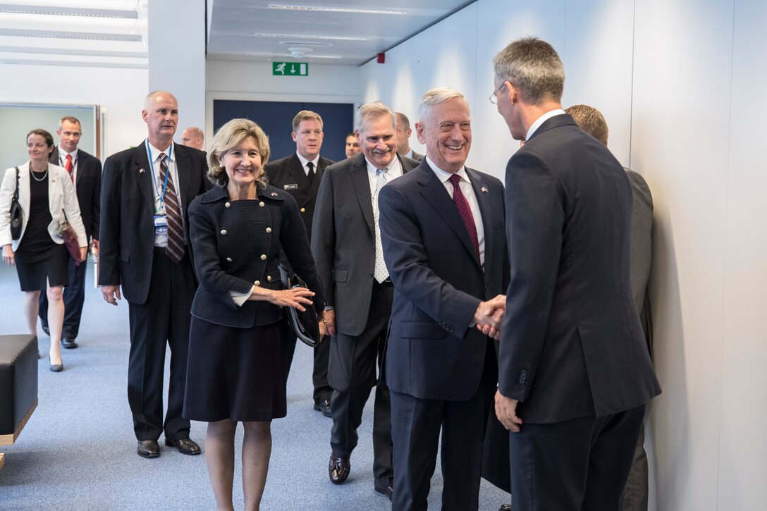 Defense Secretary James N. Mattis shakes hands with NATO Secretary Genreral Jens Stoltenberg in a hallway, with other officials behind them.