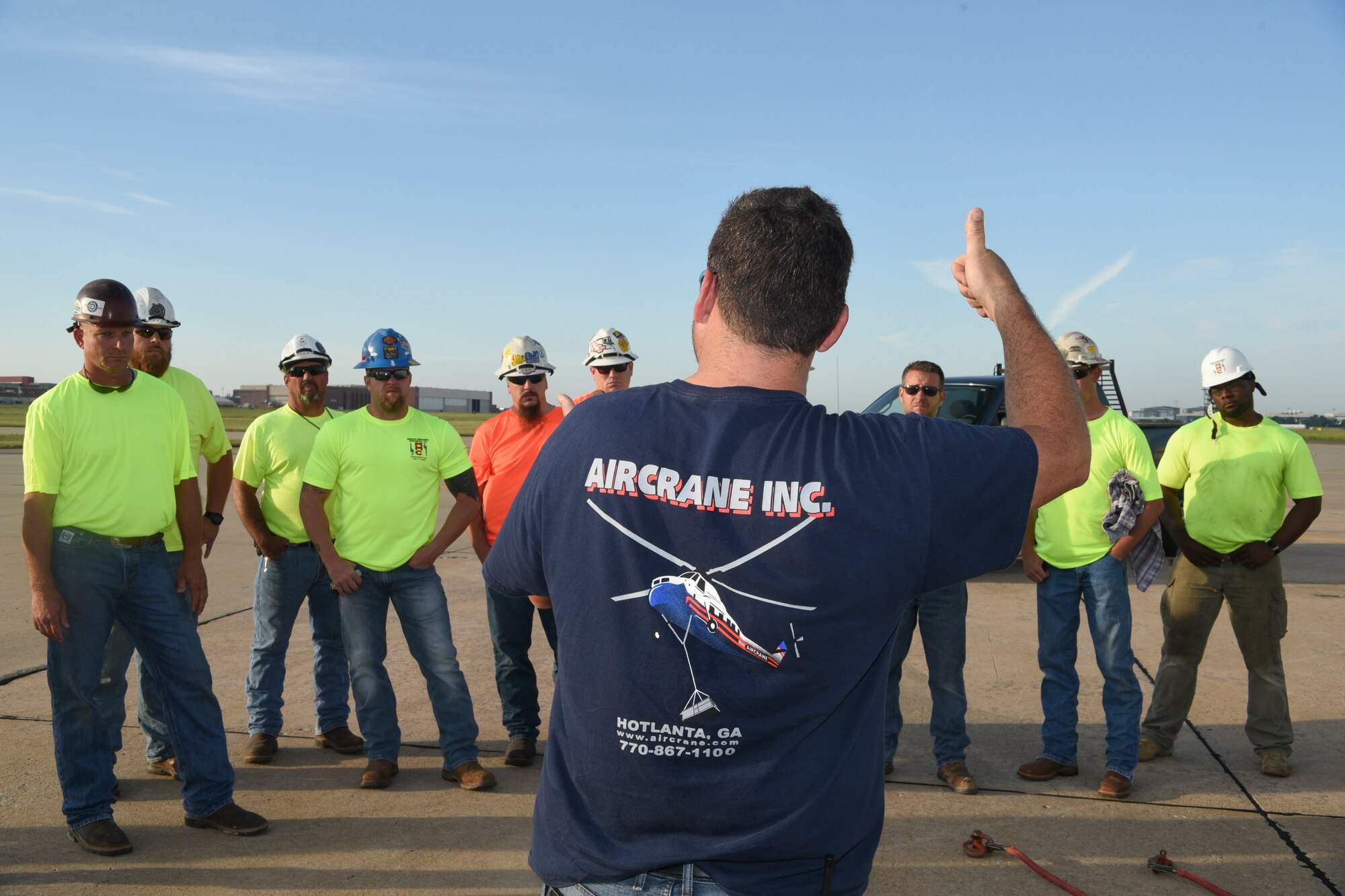 Jamey Culverson, a heavy-lift specialist with Aircrane Incorporated, briefs trademen from Matherly Mechanical contractors on safe operations under or near Aircrane's Sikorsky S-58T heavy-lift helicopter before the planned move of 57 heating units to the roof of building 3001 May 27, 2018, Tinker Air Force Base, Oklahoma.