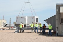 Tradesmen from Matherly Mechanical contractors position a large heating unit over a support frame while it is lowered in to place by a Sikorsky S-58T heavy-lift helicopter from Aircrane Incorporated May 27, 2018, Tinker Air Force Base, Oklahoma.