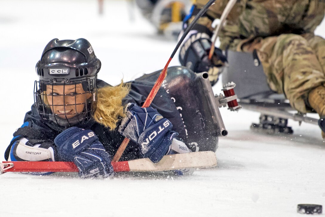 An athlete on a sled falls over while taking a shot on the ice.