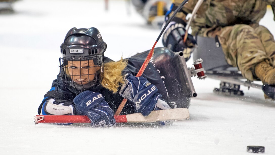 An athlete on a sled falls over while taking a shot on the ice.