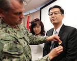 Capt. Scott Kraft, NSWC IHEODTD commanding officer, pins the Secretary of Defense Medal for Meritorious Civilian Service on Steve Kim, as his wife Julianne Kim watches on, at a ceremony held at NSWC Indian Head EOD Technology Division on 7 June 2018.