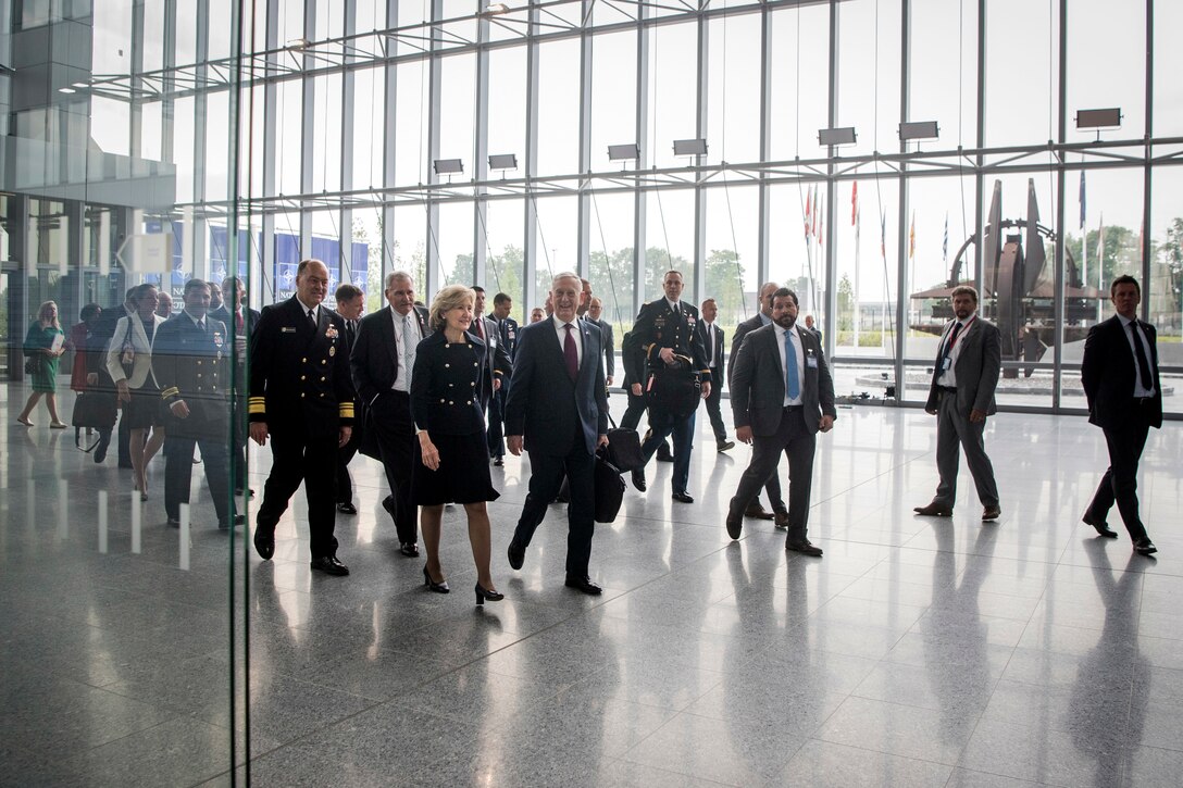 Defense Secretary James N. Mattis and a group of officials walk in an expansive building lobby with glass walls.