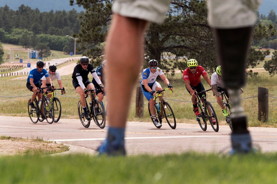 A veteran stands near the race course watching competitors participating in a cycling event.