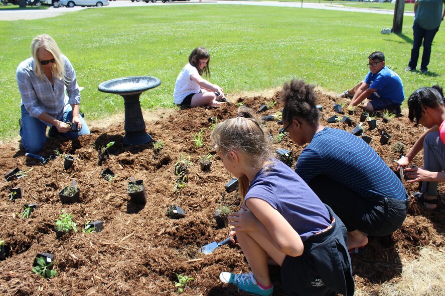 Danielle Trevino, Environmental Protection specialist, top left, helps children from the Youth Center build a monarch waystation. The Natural Resources division is creating two monarch waystations at different locations to help provide habitats necessary for monarch conservation. (U.S. Air Force photo/Stacey Geiger)