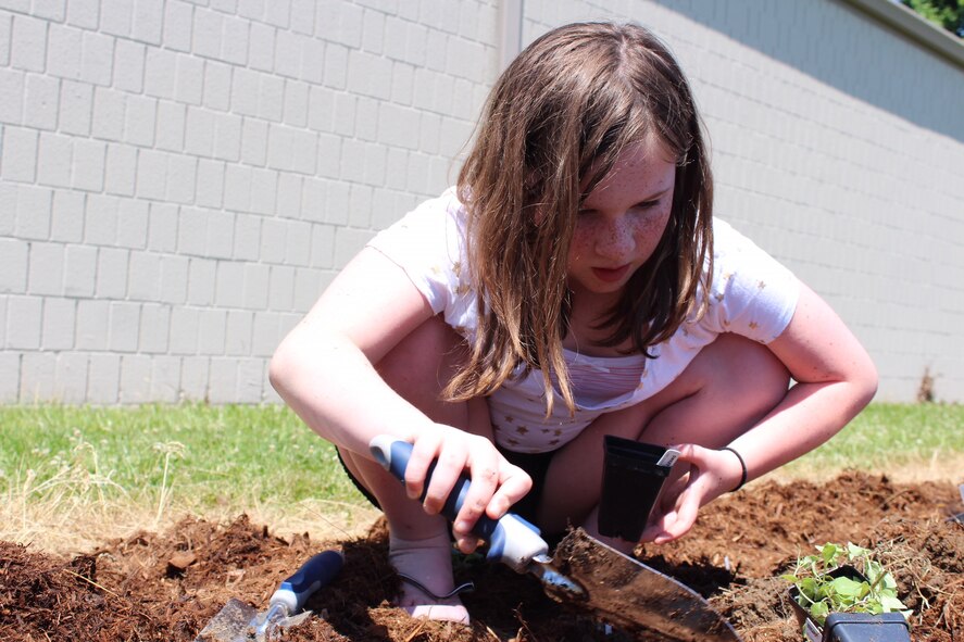 Raya Mills, 10, plants a monarch-friendly plant for the monarch waystation. While learning about the importance of preserving the pollinator population, children at the youth center helped build a monarch waystation. They will then maintain the waystation throughout the year. (U.S. Air Force photo/Stacey Geiger)