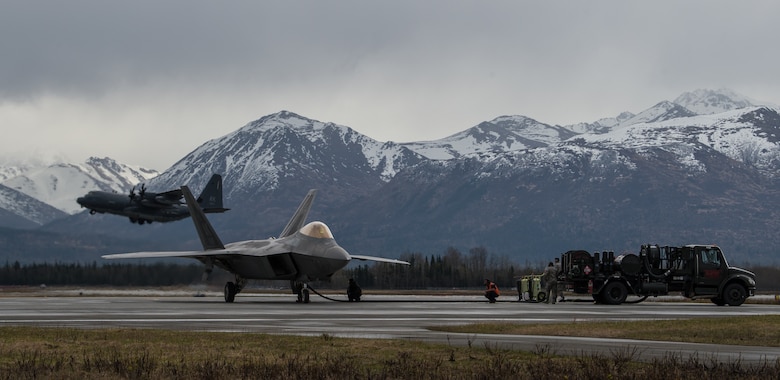 An F-22 Raptor refuels while a C-130 Hercules takes off at Joint Base Elmendorf-Richardson, Alaska, May 10, 2018. The Raptor performs both air-to-air and air-to-ground missions allowing full realization of operational concepts vital to the 21st century Air Force. The C-130 can accommodate a wide variety of oversized cargo, including utility helicopters and six-wheeled armored vehicles to standard palletized cargo and passengers.