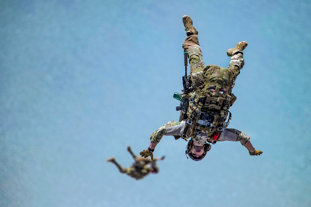 Two airmen appear to float midair in blue sky before opening their parachutes.