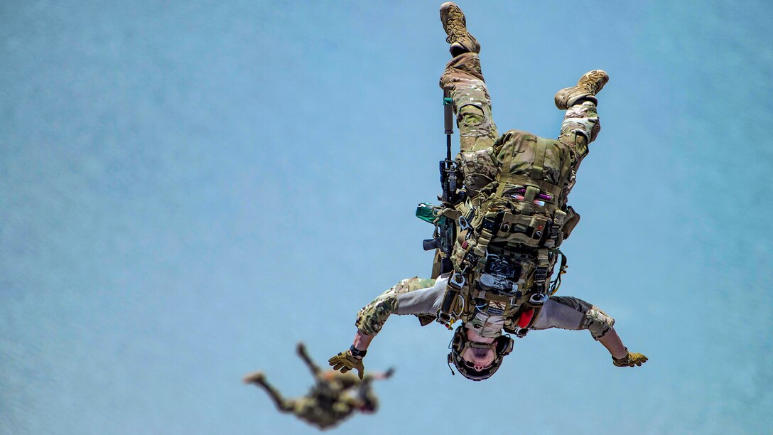 Two airmen appear to float midair in blue sky before opening their parachutes.