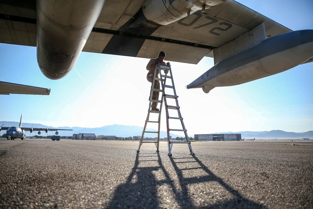 A Marine climbs a ladder beneath the wing of an aircraft on a flightline.