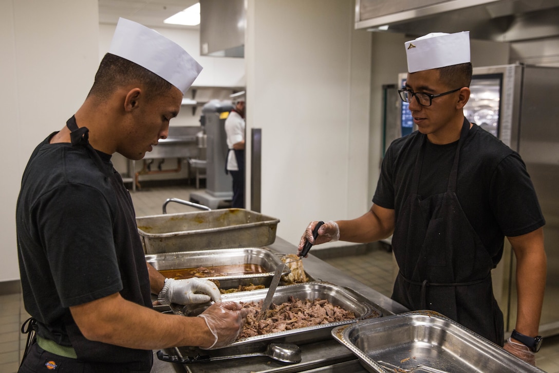 Lance Cpl. Tanielu Boycejennings, food service specialist, 3rd Battalion, 7th Marine Regiment, and Lance Cpl. Hector Zamora, food service specialist, Headquarters Battalion, prepare pork for the Phelps Mess Hall grand re-opening aboard the Marine Corps Air Ground Combat Center, Twentynine Palms, Calif., June 4, 2018.  Phelps Hall has been closed since November 11, 2017, due to renovations to improve the efficiency of the facility. (U.S. Marine Corps photo by Lance Cpl. Margaret Gale)