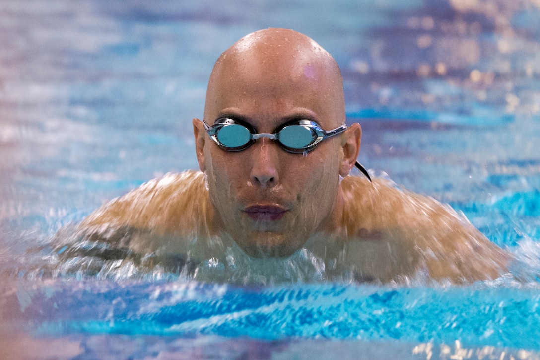 An airman wearing goggles swims in a pool.