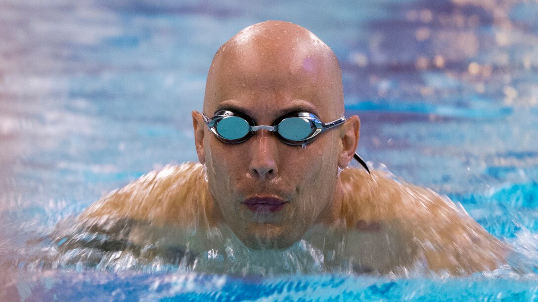 An airman wearing goggles swims in a pool.
