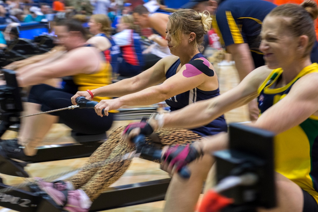 Athletes on indoor rowing machines compete in a gym.