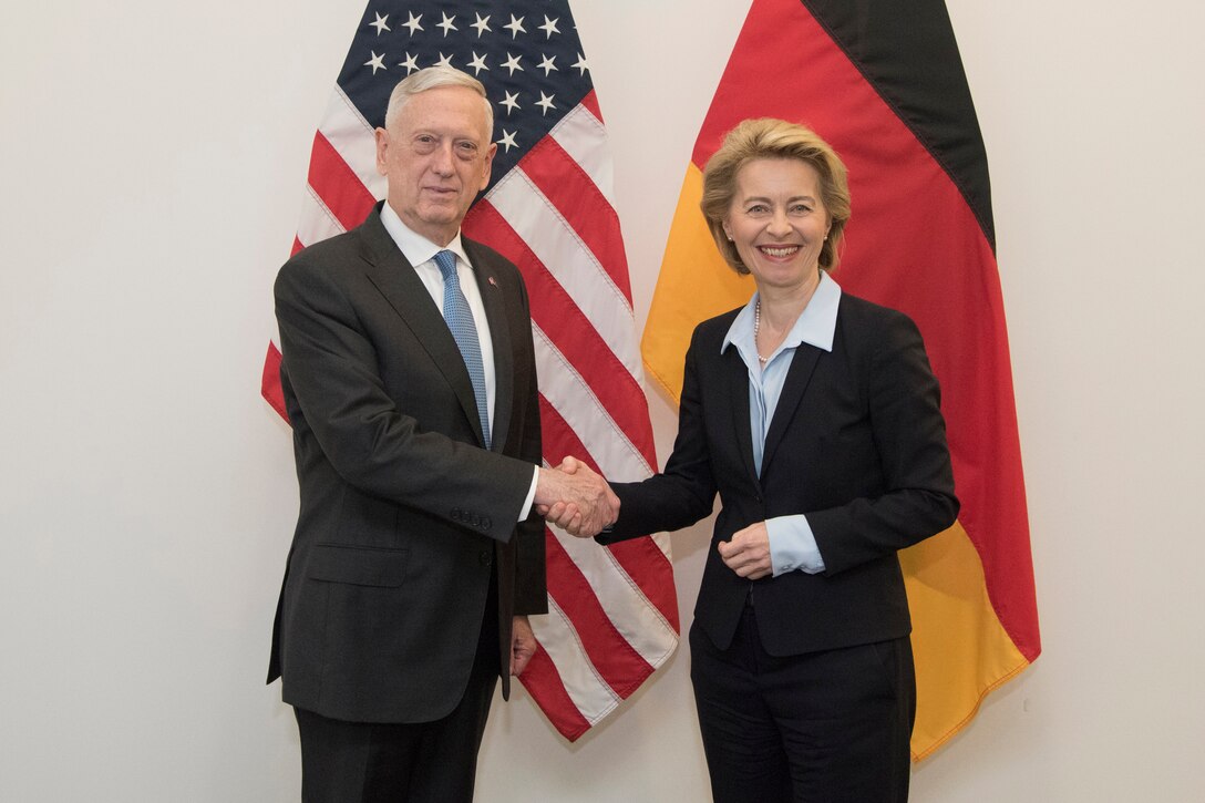 Defense Secretary James N. Mattis shakes hands with his German counterpart as they pose in front of their nations' flags.