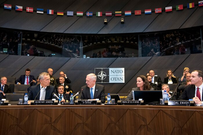 Defense Secretary James N. Mattis talks with fellow defense ministers while sitting at a table in a NATO meeting room.