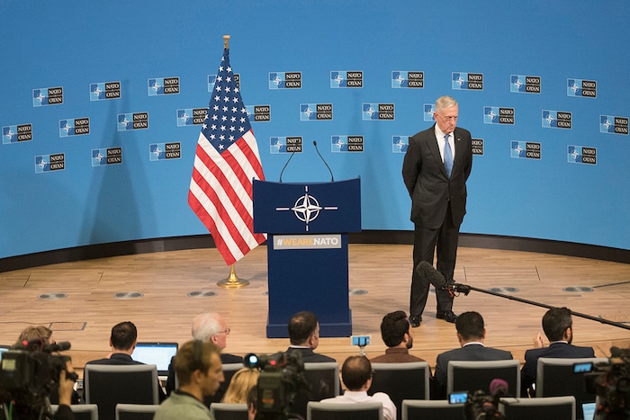 Defense Secretary James N. Mattis stands on a stage beside a lectern while speaking to reporters.